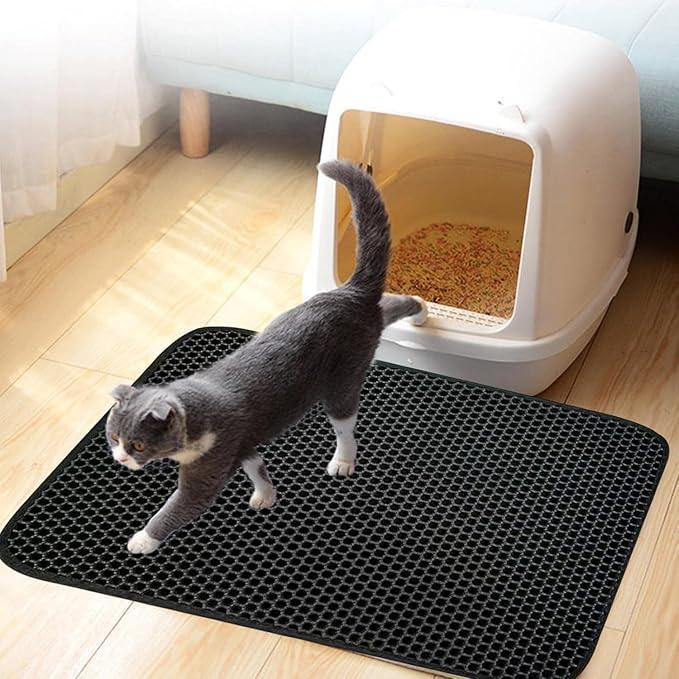 Gray cat walking on black litter mat near enclosed cat litter box on wooden floor
